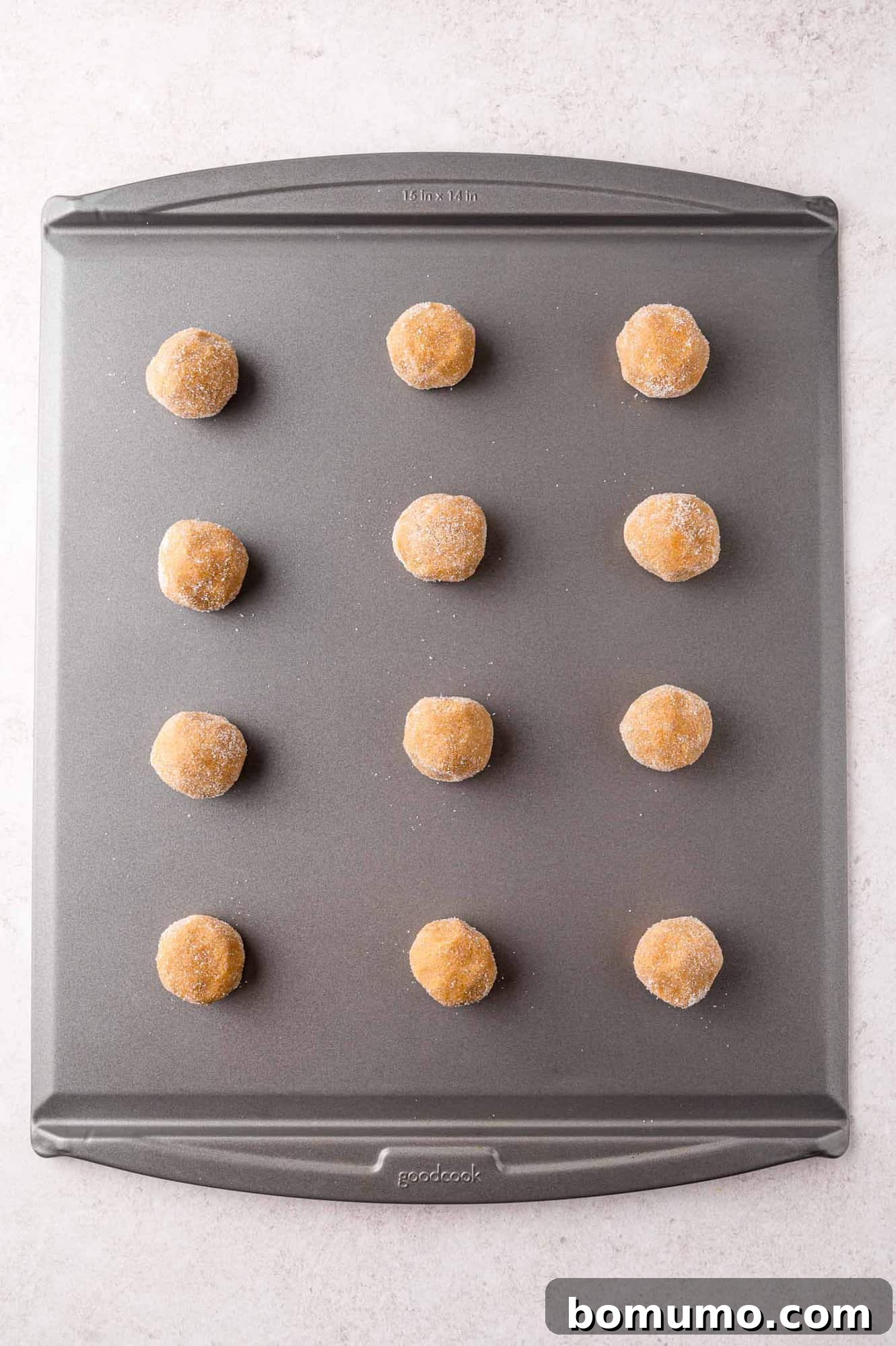 Twelve evenly spaced cookie dough balls, generously coated in sugar, arranged on a baking sheet, ready for the oven.