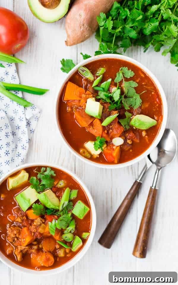 Overhead view of two bowls of Instant Pot chili, garnished with cubed avocado, chopped green onion, and fresh cilantro, suggesting a wholesome and appetizing meal.