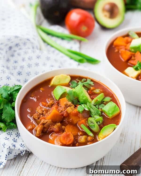 A close-up shot of a single serving of hearty chili in a round white bowl, beautifully garnished, emphasizing its rich texture and inviting presentation.