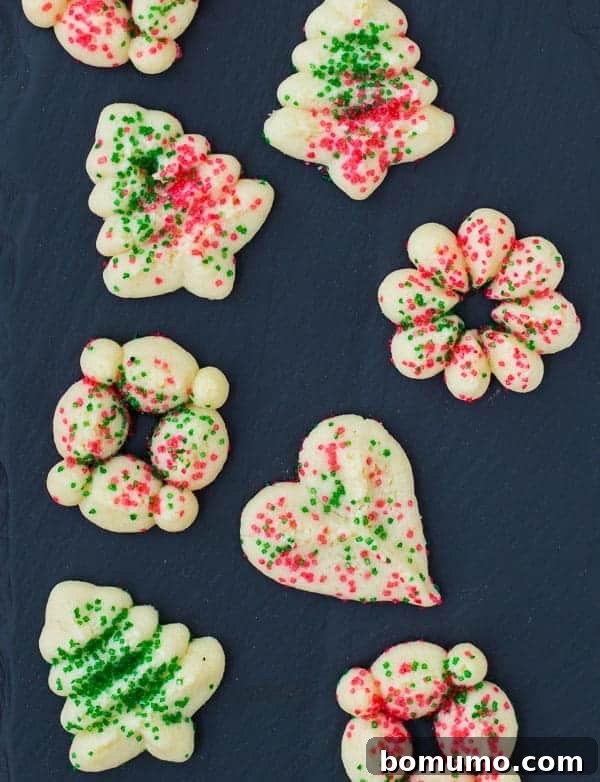 Overhead view of several spritz cookies in a variety of intricate shapes on a dark slate background, showcasing their decorative appeal.