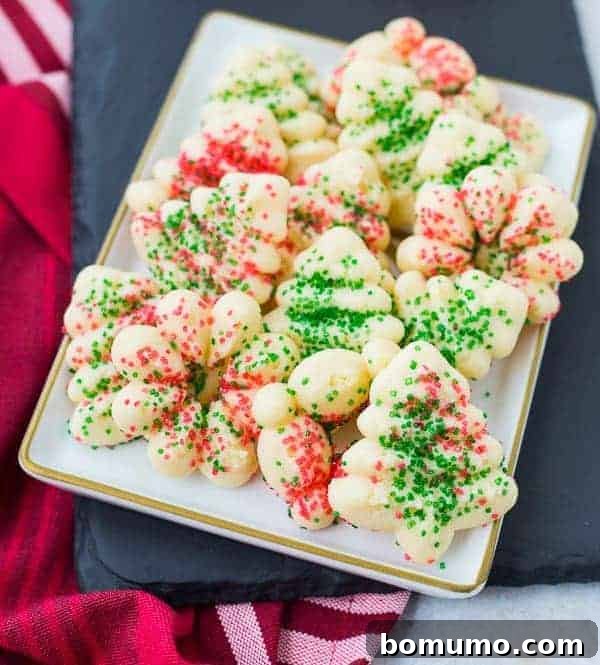Several decorated spritz cookies artfully arranged on a rectangular white plate, showcasing their festive appeal.