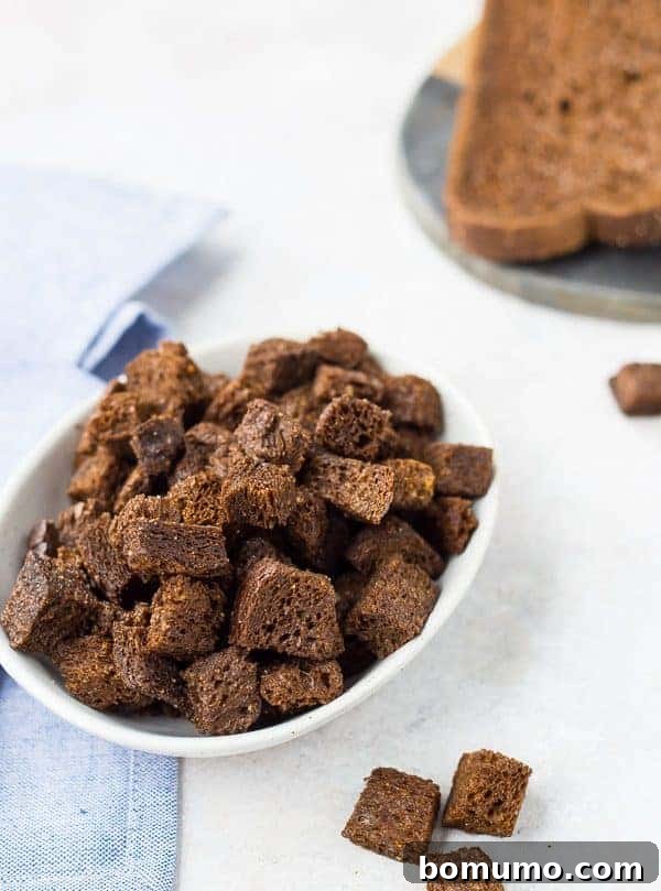 Freshly baked pumpernickel croutons spread on a baking sheet, golden and crisp, showcasing their delicious texture and readiness to be enjoyed.