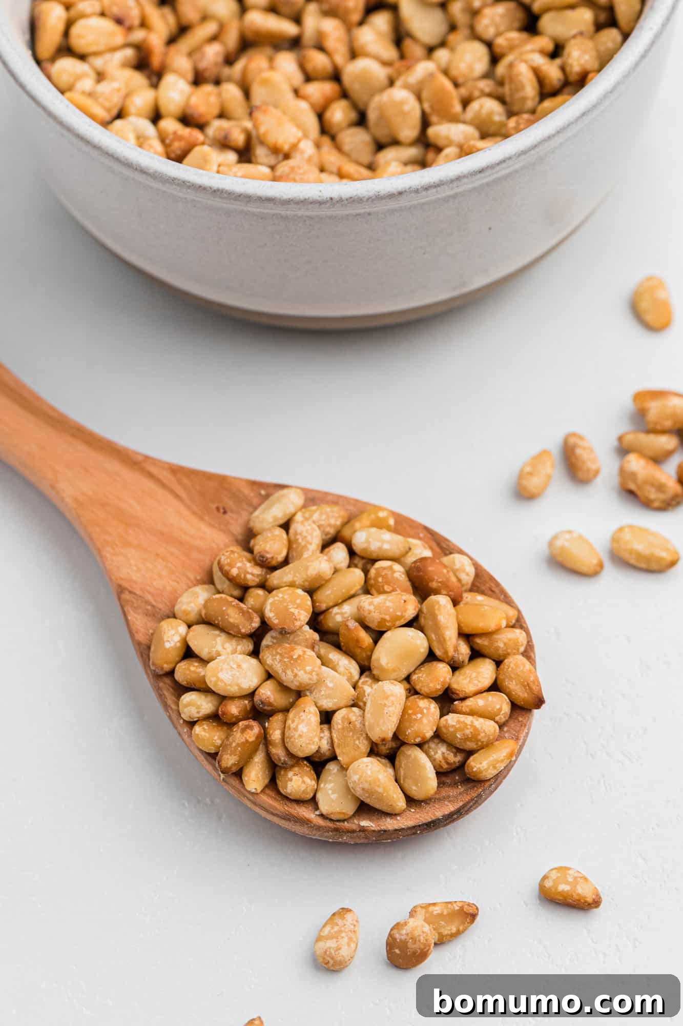 Toasted pine nuts on a small wooden spoon, showcasing their beautiful golden color.