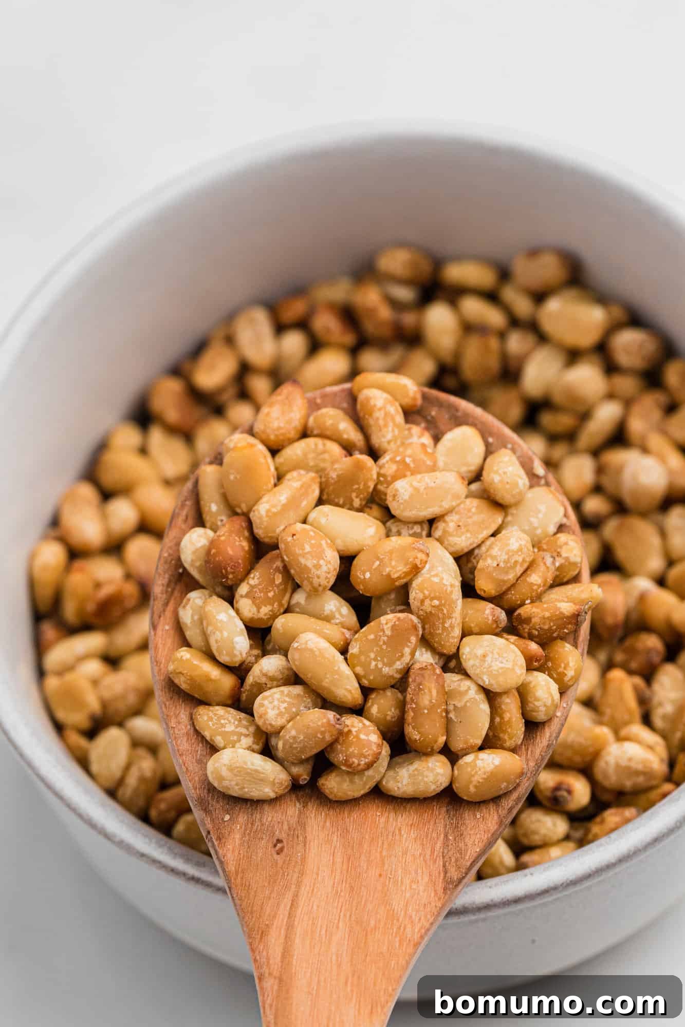 Perfectly golden toasted pine nuts in a small white bowl, ready for use.