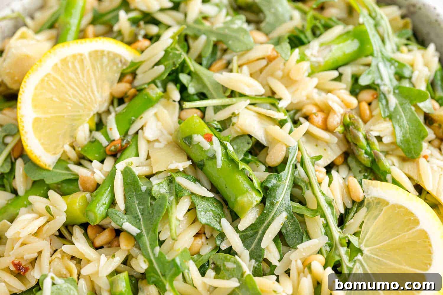 Close up view of orzo salad garnished with lemon wedges.