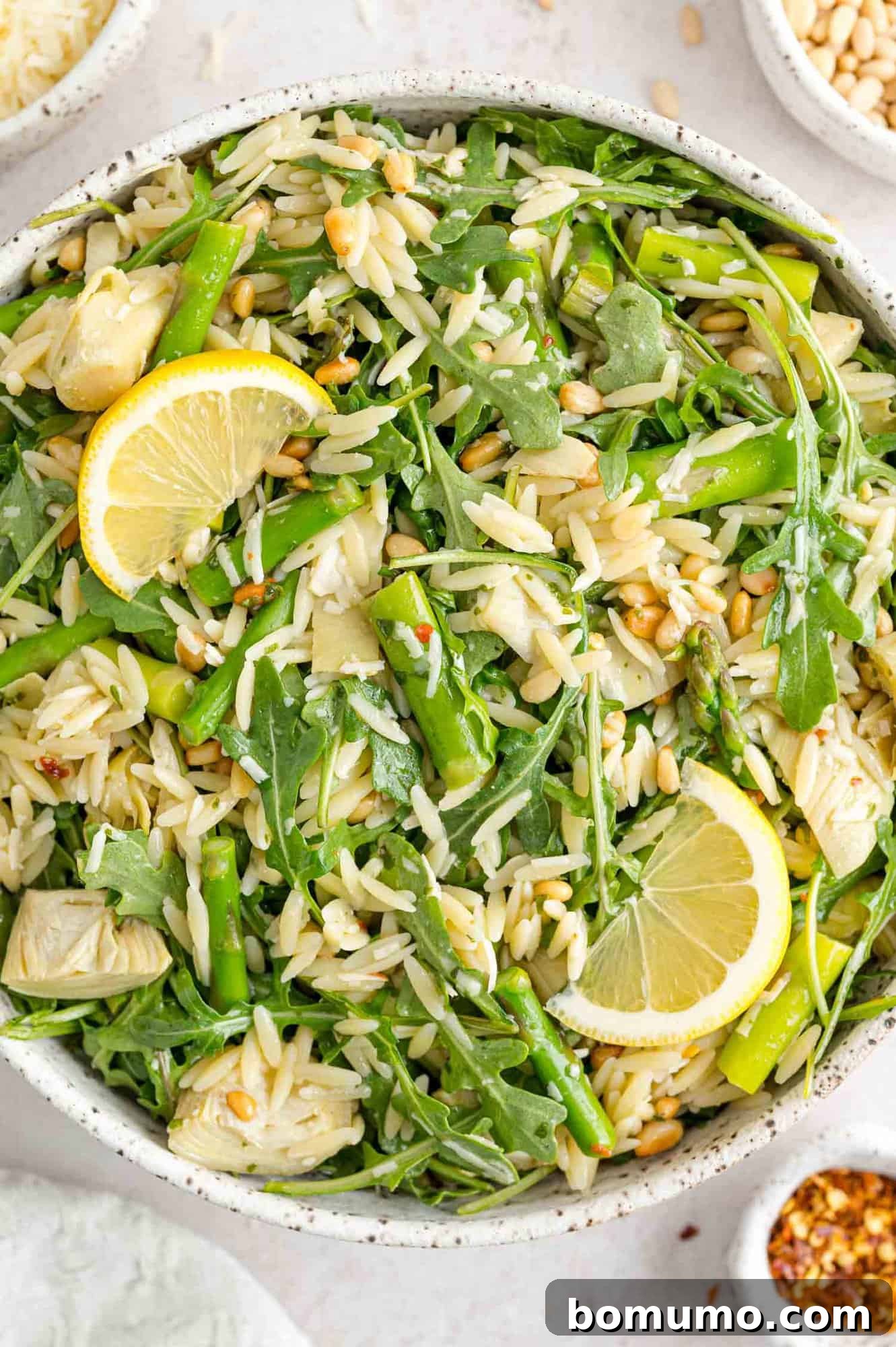 Orzo salad with asparagus, lemon, and pine nuts in large white bowl.