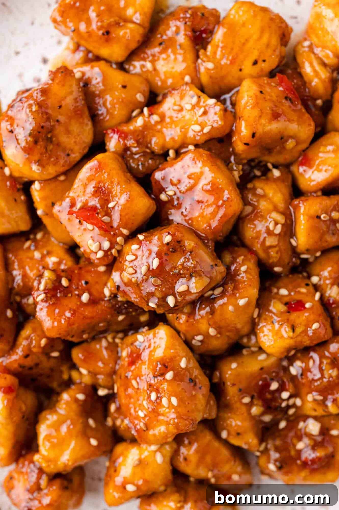 Close-up of glazed, golden-brown chicken bites sprinkled with sesame seeds.