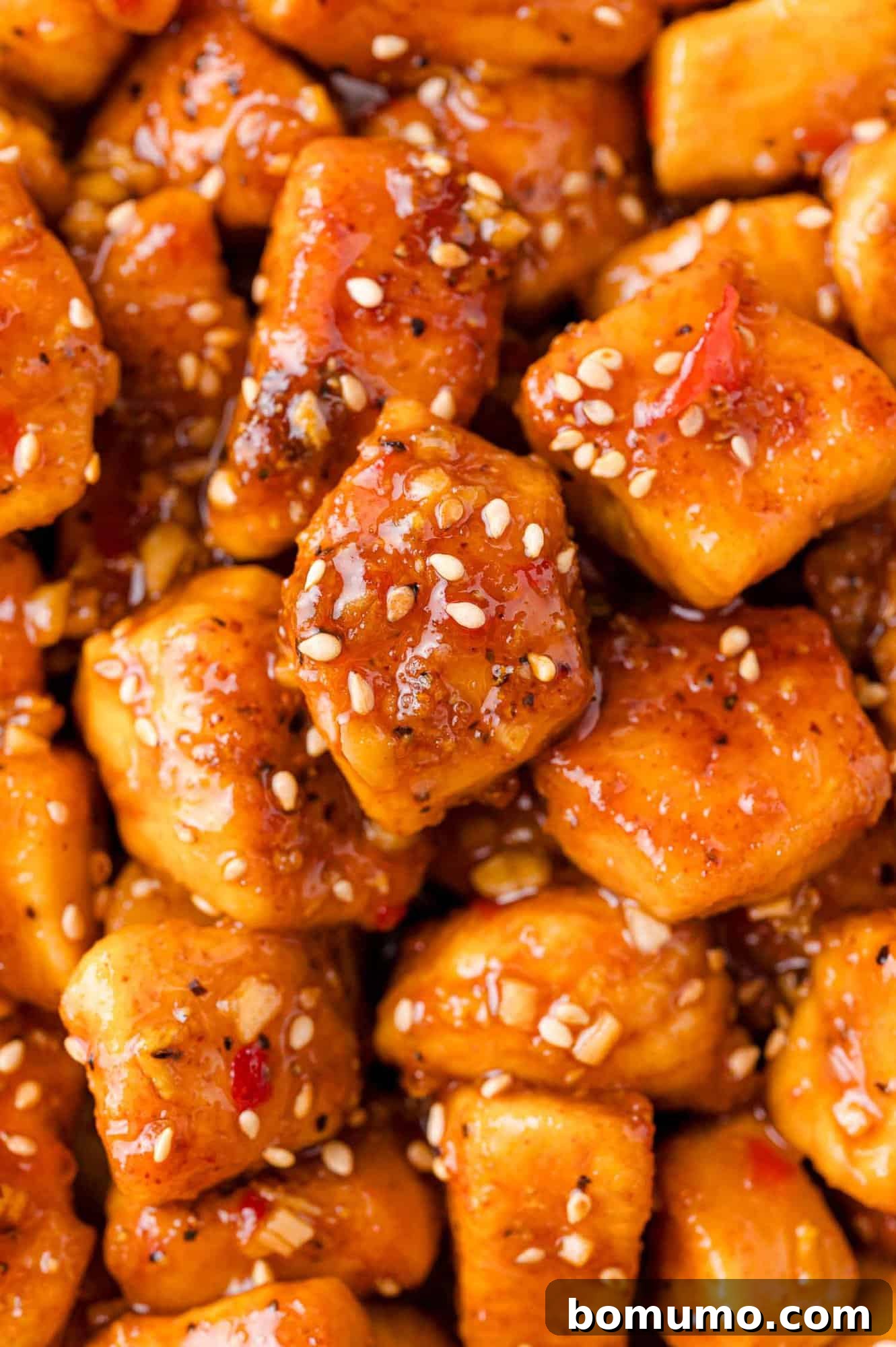 Close-up of cubed chicken coated in a glossy sauce with sesame seeds sprinkled on top.
