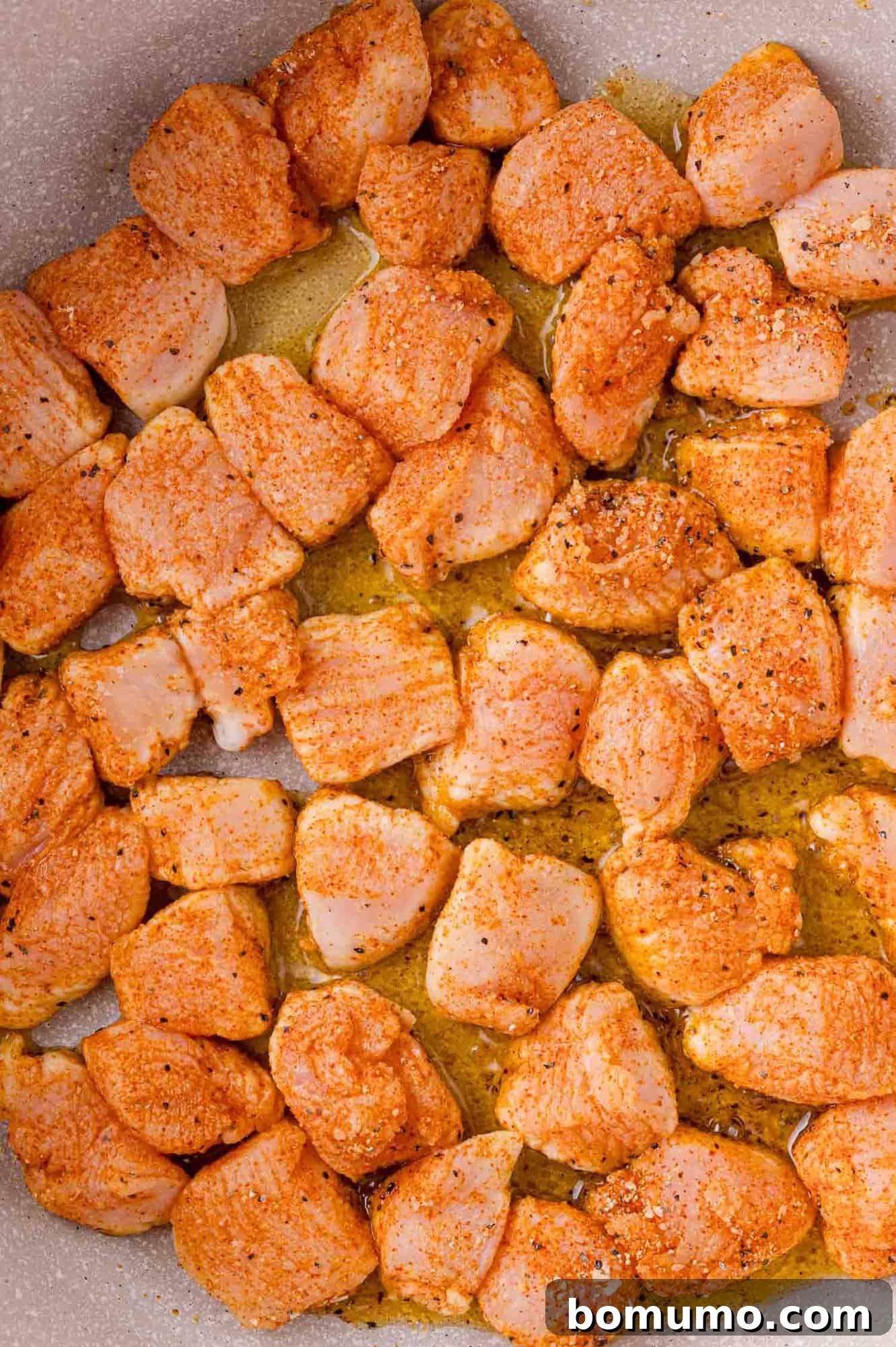 Close-up of cubed chicken pieces seasoned and cooking in a pan with oil.