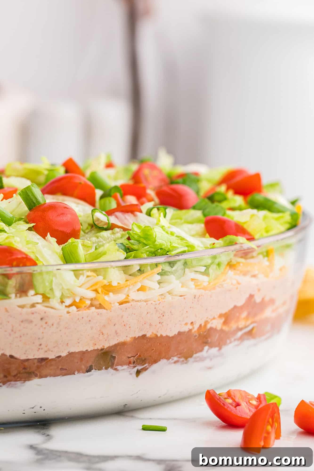 Seven-Layer Fiesta Dip 3 A transparent glass dish showcasing the perfectly distinct and colorful 7 layers of the exceptional dip, ready to be served.