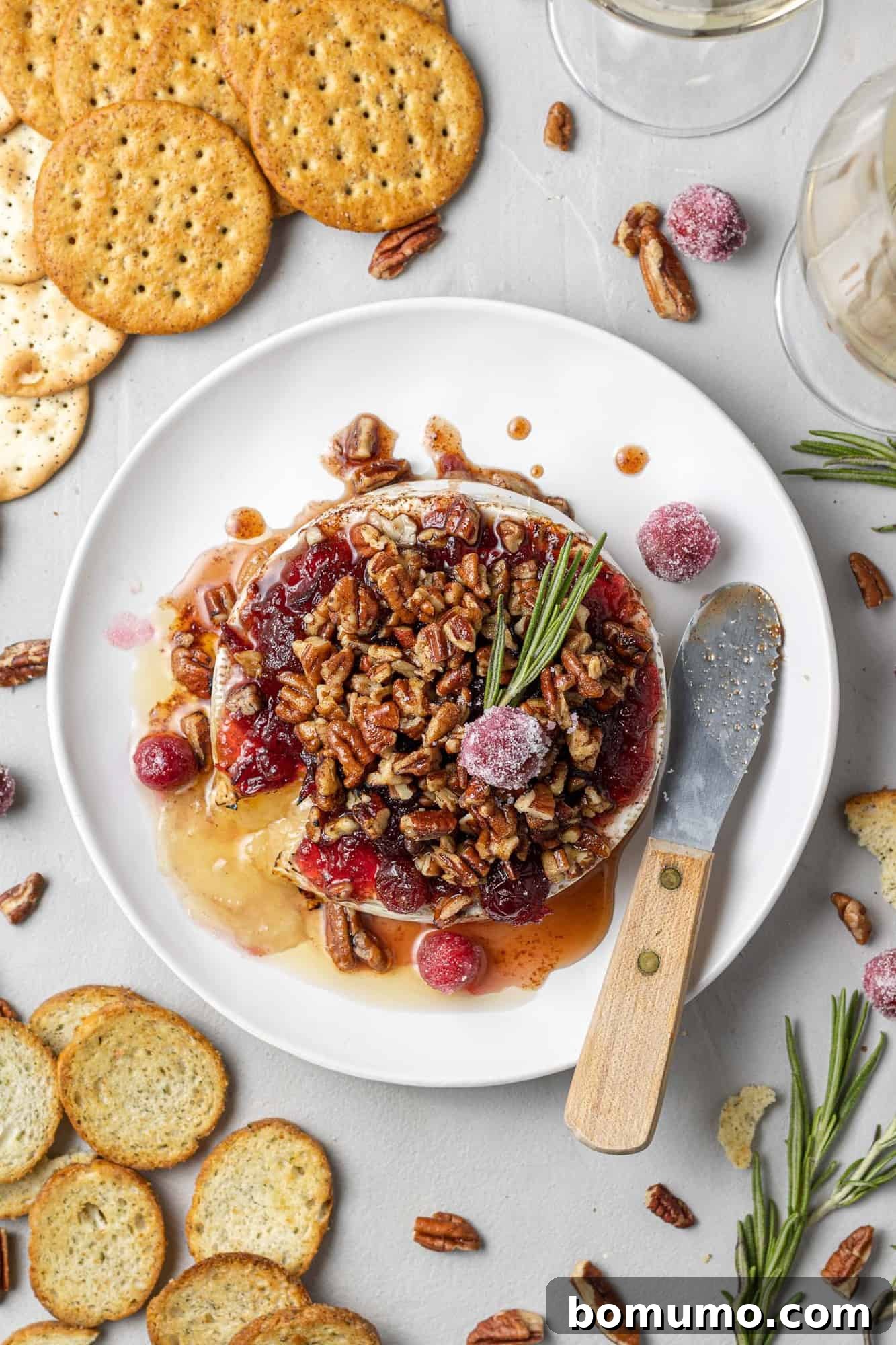 Overhead view of brie topped with cranberries and pecans, garnished with fresh rosemary.