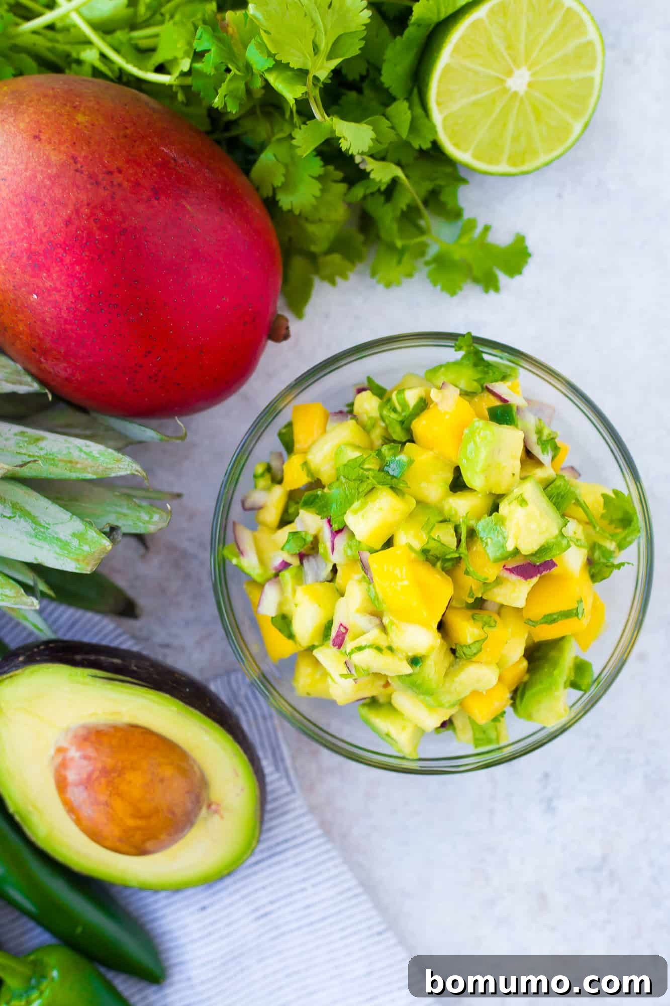 Mango Avocado Pineapple Fiesta 2 A small glass bowl filled with vibrant mango avocado salsa, featuring chunks of ripe mango, creamy avocado, and fresh herbs.