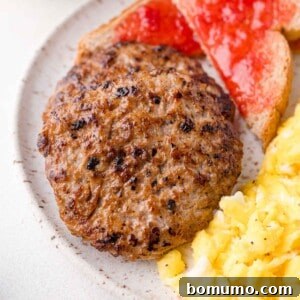Two cooked sausage patties on a plate with scrambled eggs and toast topped with red jam.