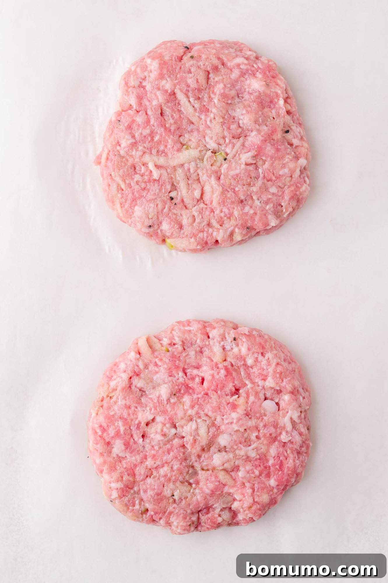 Two raw ground meat patties on a white surface, spaced apart and ready for cooking.