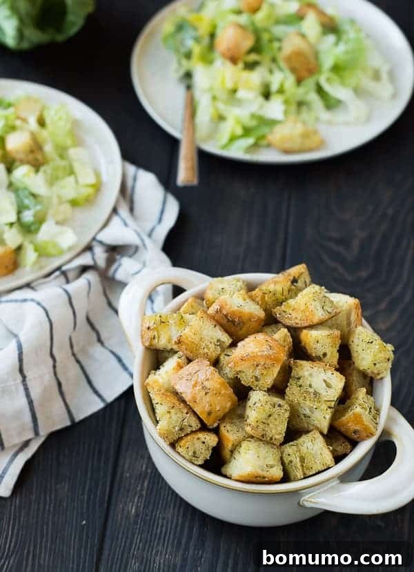 Homemade Caesar Croutons: A Game-Changer for Your Salads! Learn how to make crispy, flavorful croutons that surpass any store-bought option and elevate your Caesar salad to gourmet status. Find the easy recipe on RachelCooks.com! A pristine white bowl adorned with handles, brimming with golden-brown Caesar croutons, ready to enhance any meal.