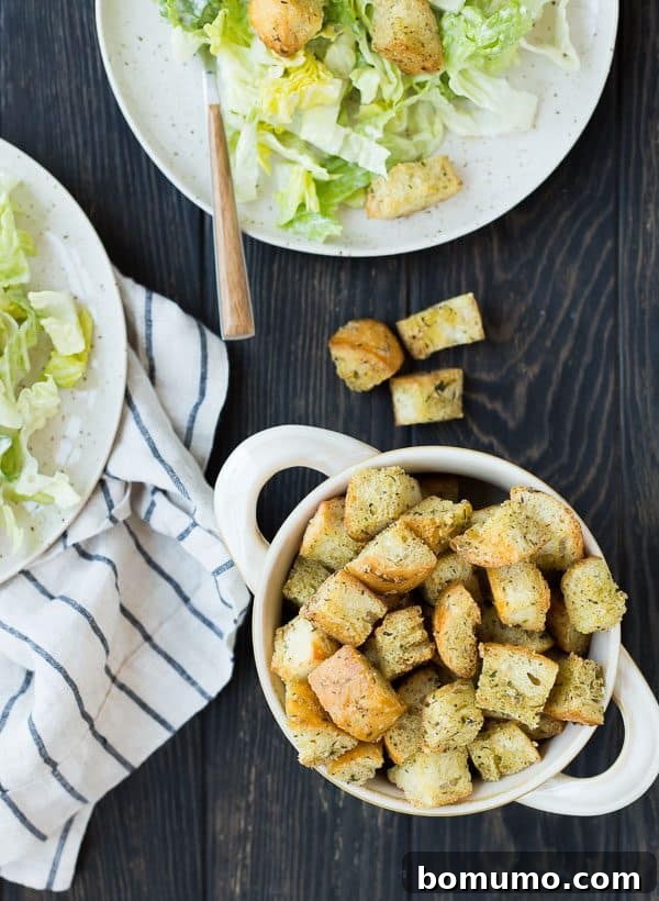 Effortless Homemade Caesar Croutons 6 An inviting overhead view of a bowl filled with perfectly toasted Caesar croutons, flanked by two fresh and vibrant Caesar salads, ready for a delicious meal.