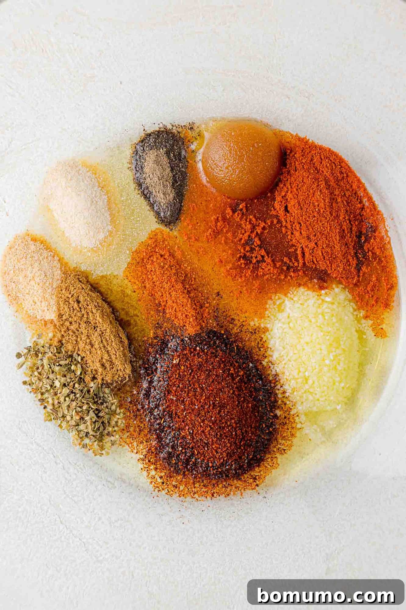 Close-up of spices and olive oil in a bowl, awaiting mixture.