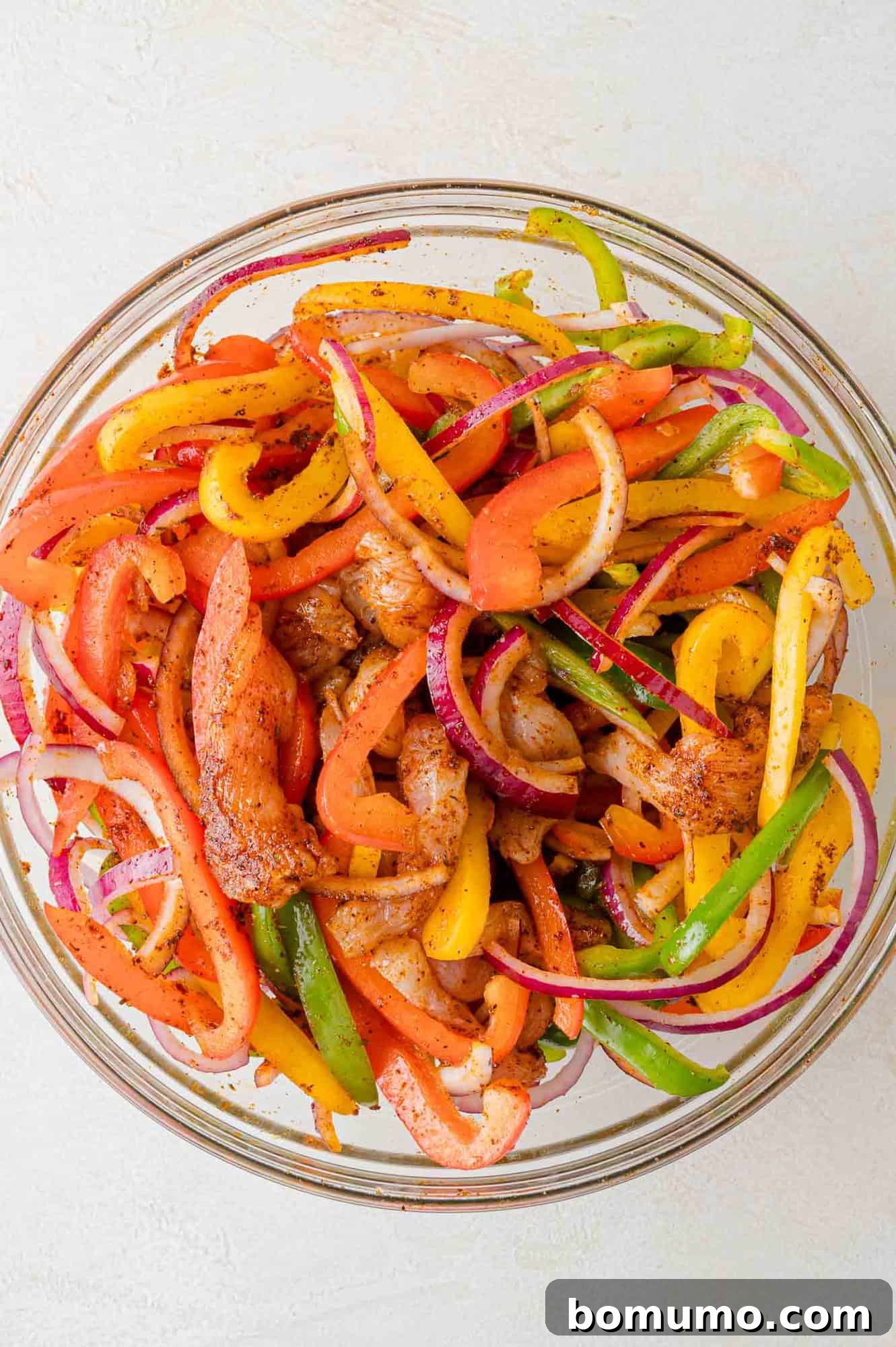 Diced chicken and vegetables perfectly coated in fajita seasoning within a mixing bowl.