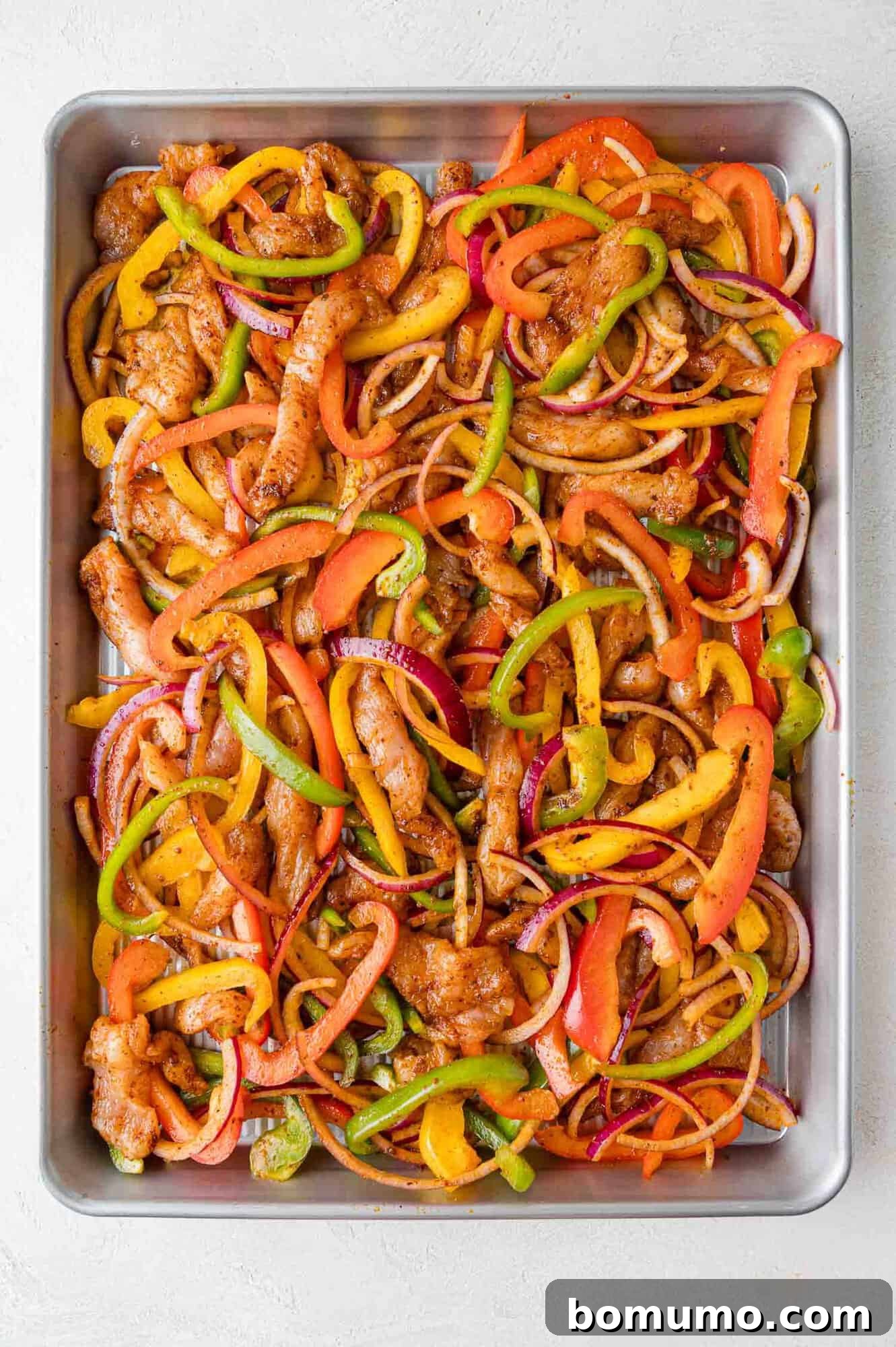 Raw fajita ingredients, chicken, peppers, and onions, arranged on a sheet pan before cooking.