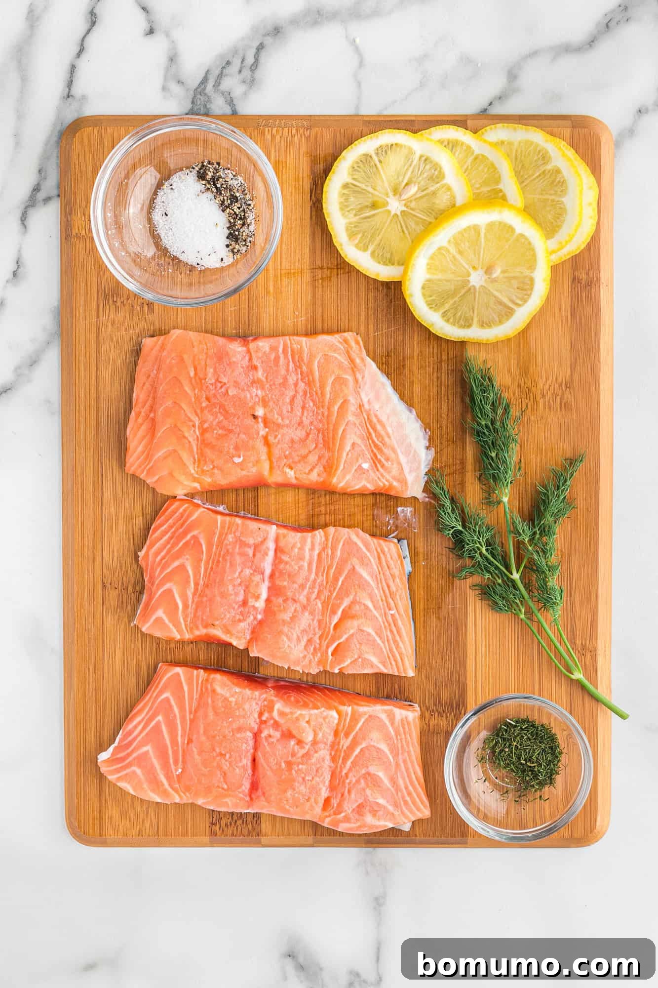 Overhead view of salmon, dill, lemon, salt and pepper.