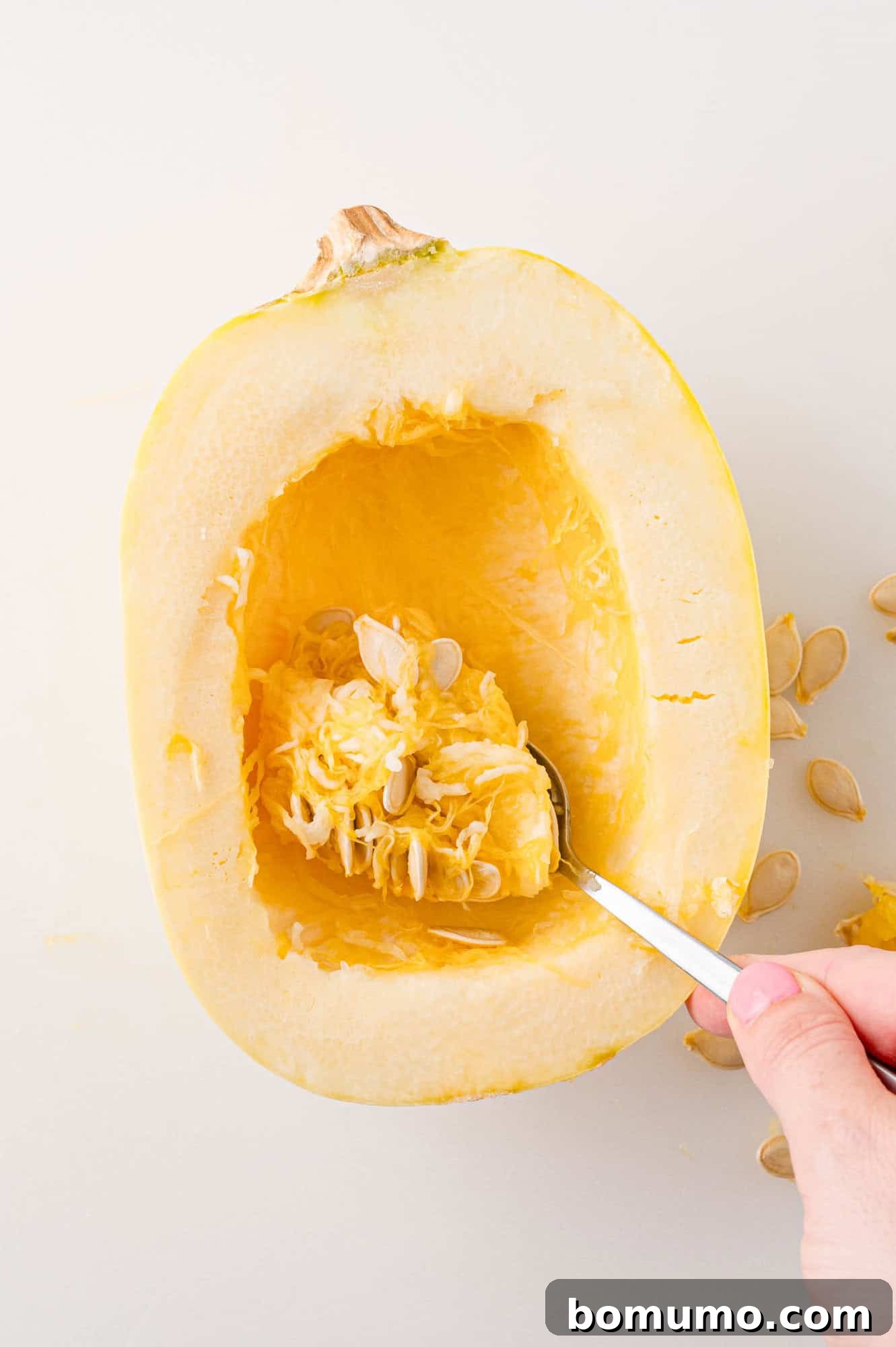 Spaghetti Squash Cooking Made Easy 11 Seeds being scooped out of uncooked spaghetti squash half.