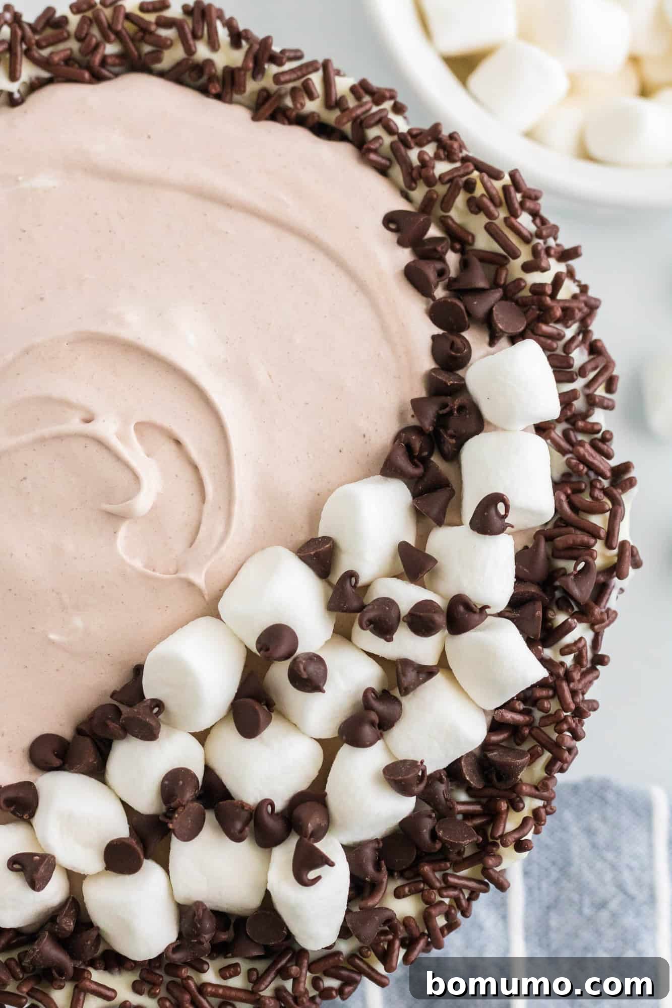 Overhead view of a sprinkle-lined bowl filled with hot chocolate dip, topped with fluffy marshmallows and decadent chocolate chips, ready for serving.