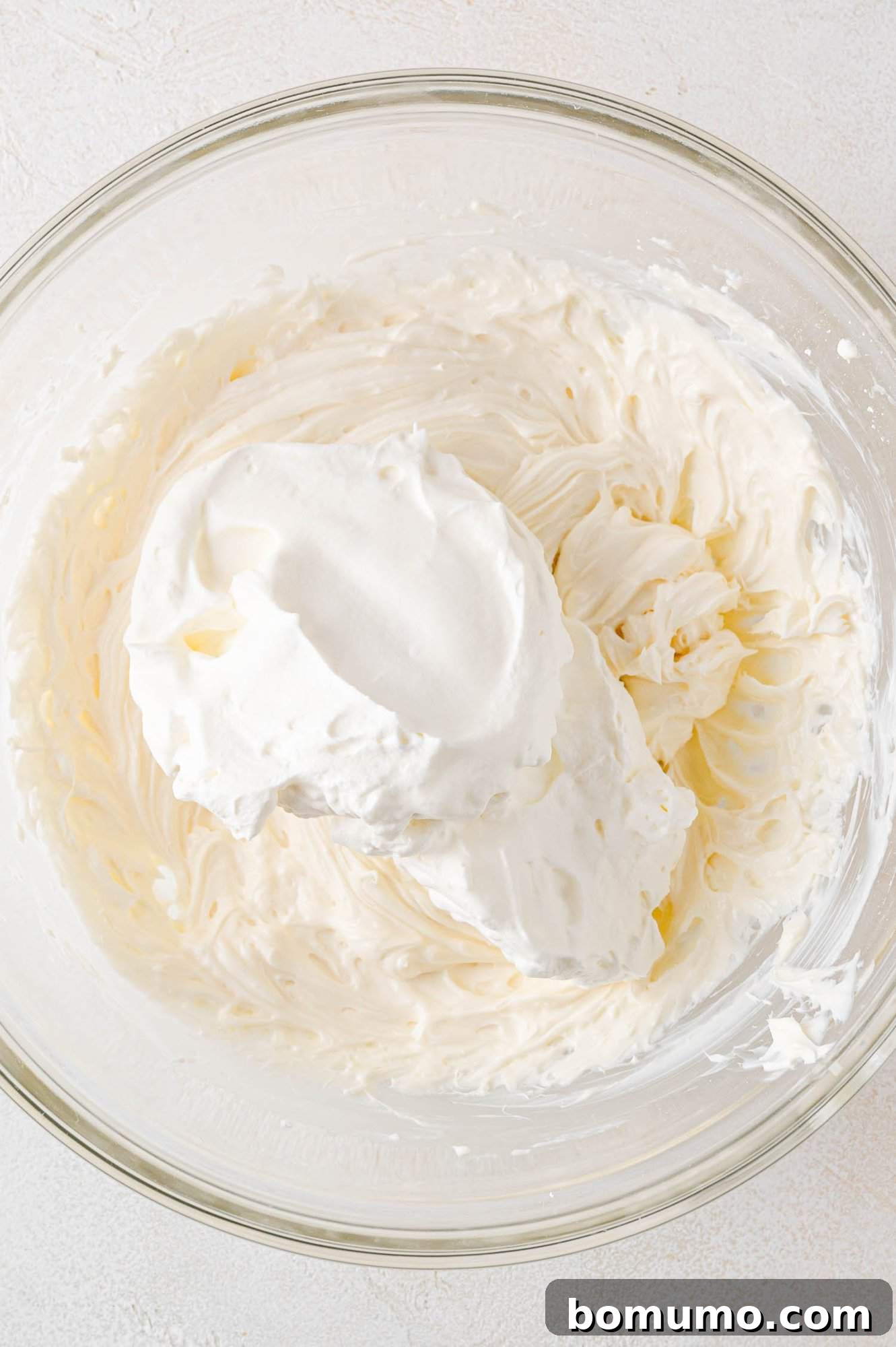 Effortless Mini Cheesecake Delights 12 A glass bowl filled with whipped cream and cream cheese mixture.