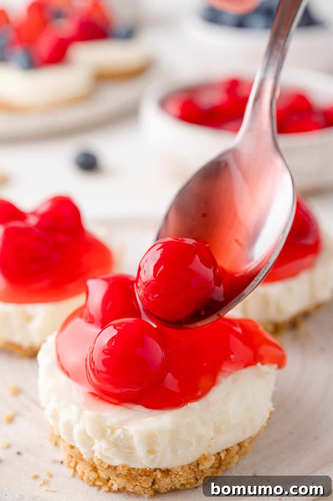 Effortless Mini Cheesecake Delights 15 A spoon places cherry topping on mini cheesecake with a crumbly base.