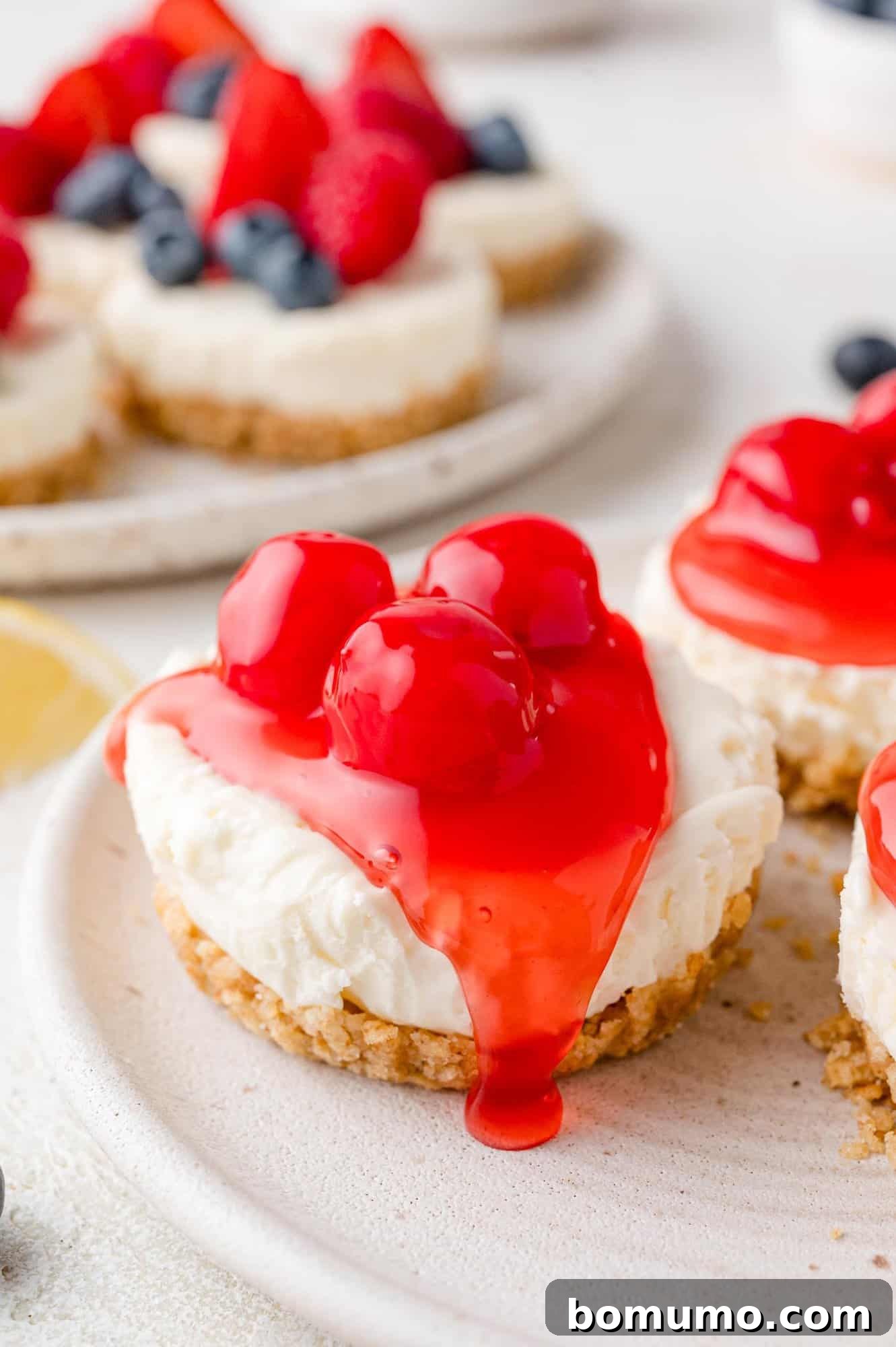 Effortless Mini Cheesecake Delights 16 Mini cheesecakes topped with glossy red cherries on a graham cracker crust, displayed on a light-colored plate.