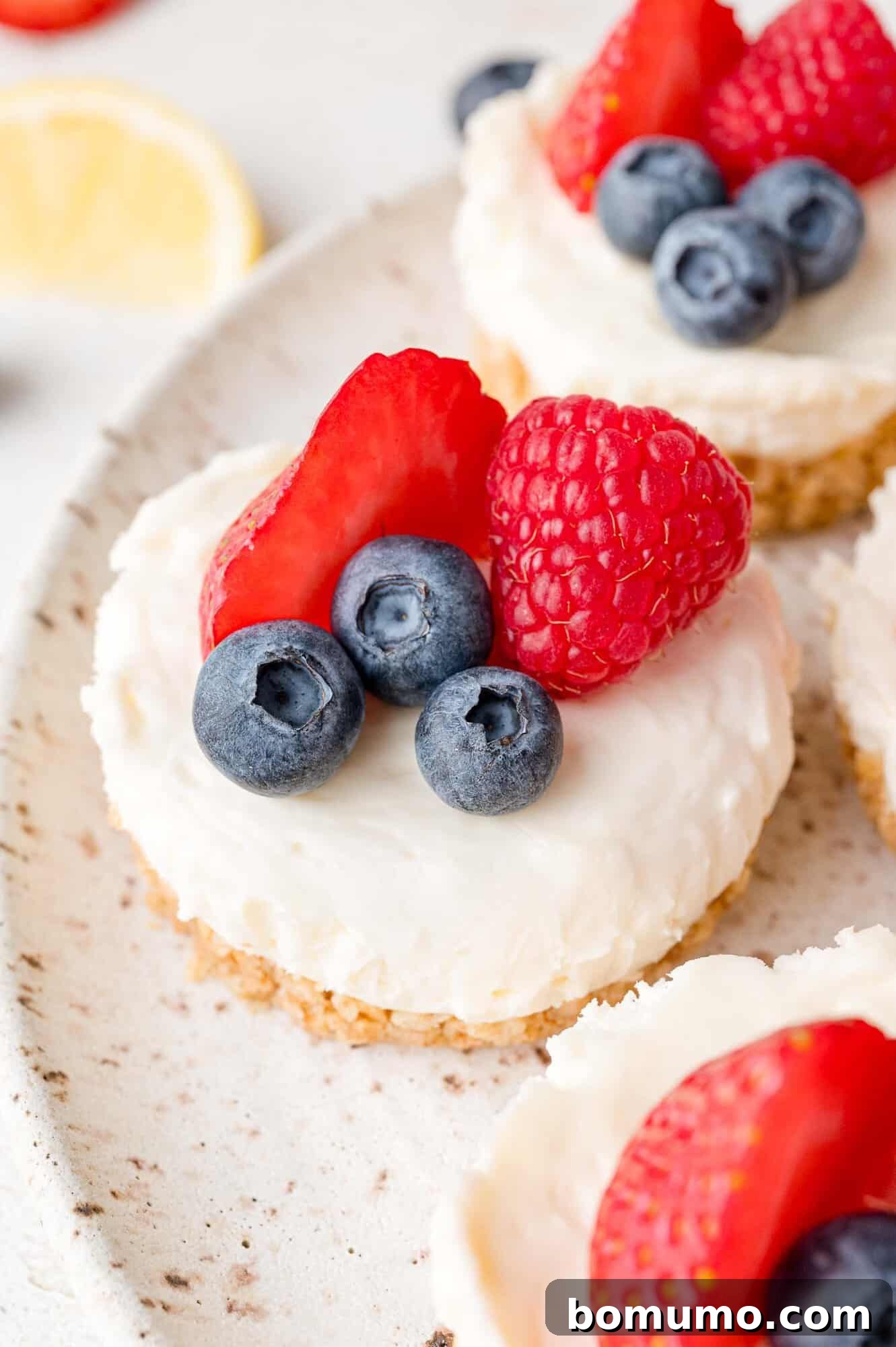 Effortless Mini Cheesecake Delights 3 Mini cheesecakes topped with blueberries, raspberries, and strawberry slices on a plate.