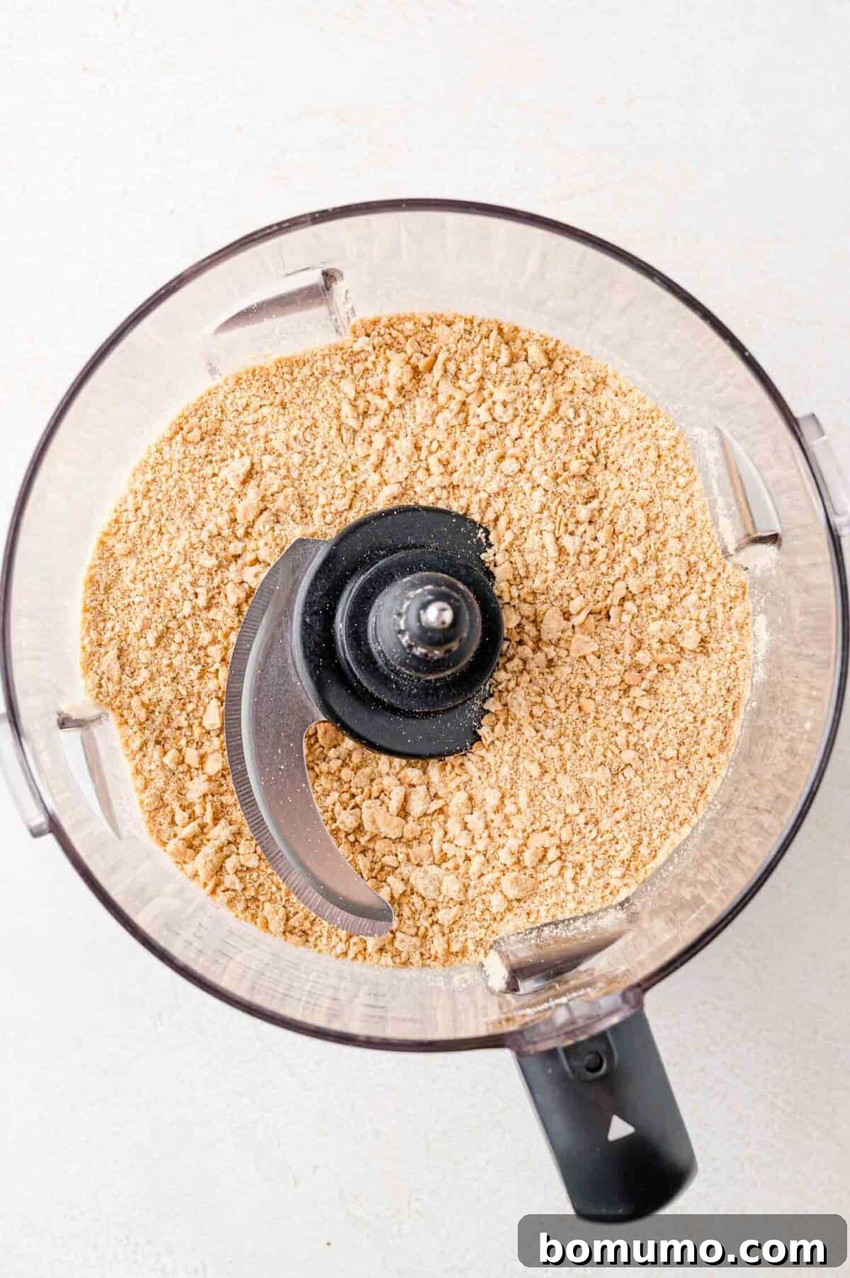 Effortless Mini Cheesecake Delights 5 Top view of a food processor bowl containing finely ground graham crackers.
