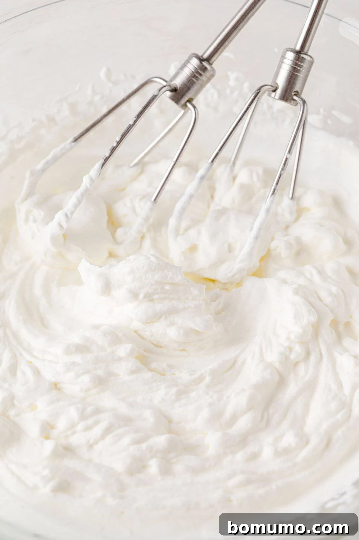 Effortless Mini Cheesecake Delights 10 Electric beaters mixing fluffy whipped cream in a glass bowl.
