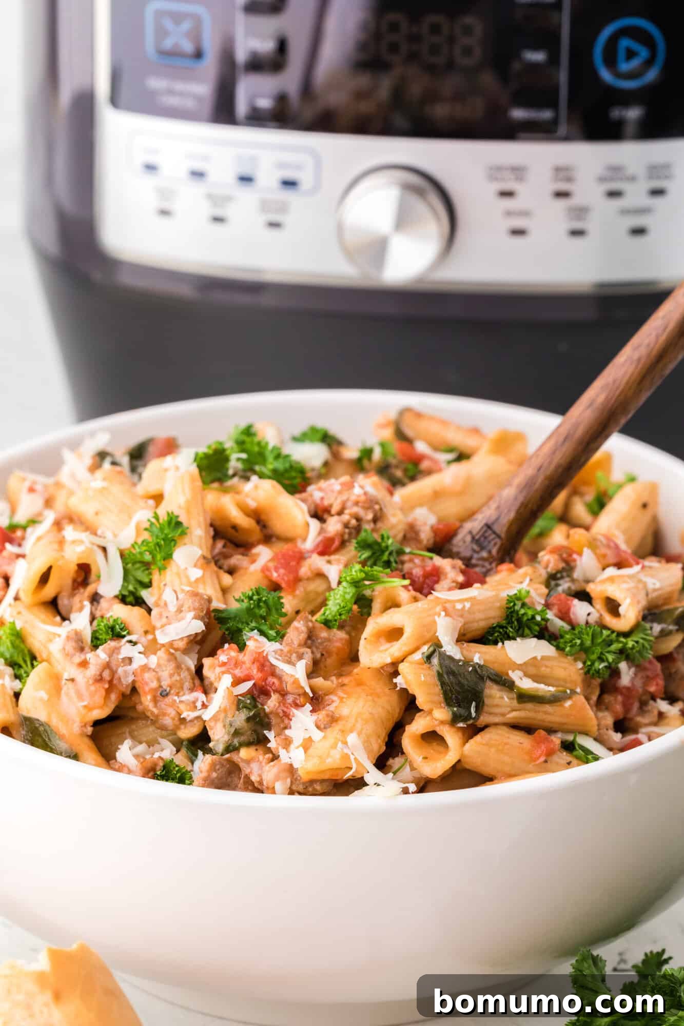 A vibrant Instant Pot pasta dish with tomatoes and spinach, positioned in front of a sleek Instant Pot appliance, ready to be served.