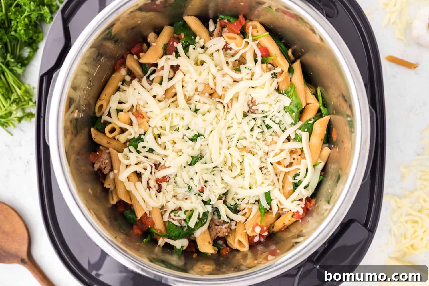 Shredded mozzarella cheese added to the hot Instant Pot pasta, preparing for its creamy transformation.
