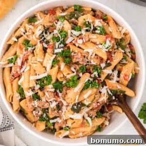 A perfectly portioned Instant Pot pasta dish with sausage, spinach, and tomatoes, presented in a white bowl.