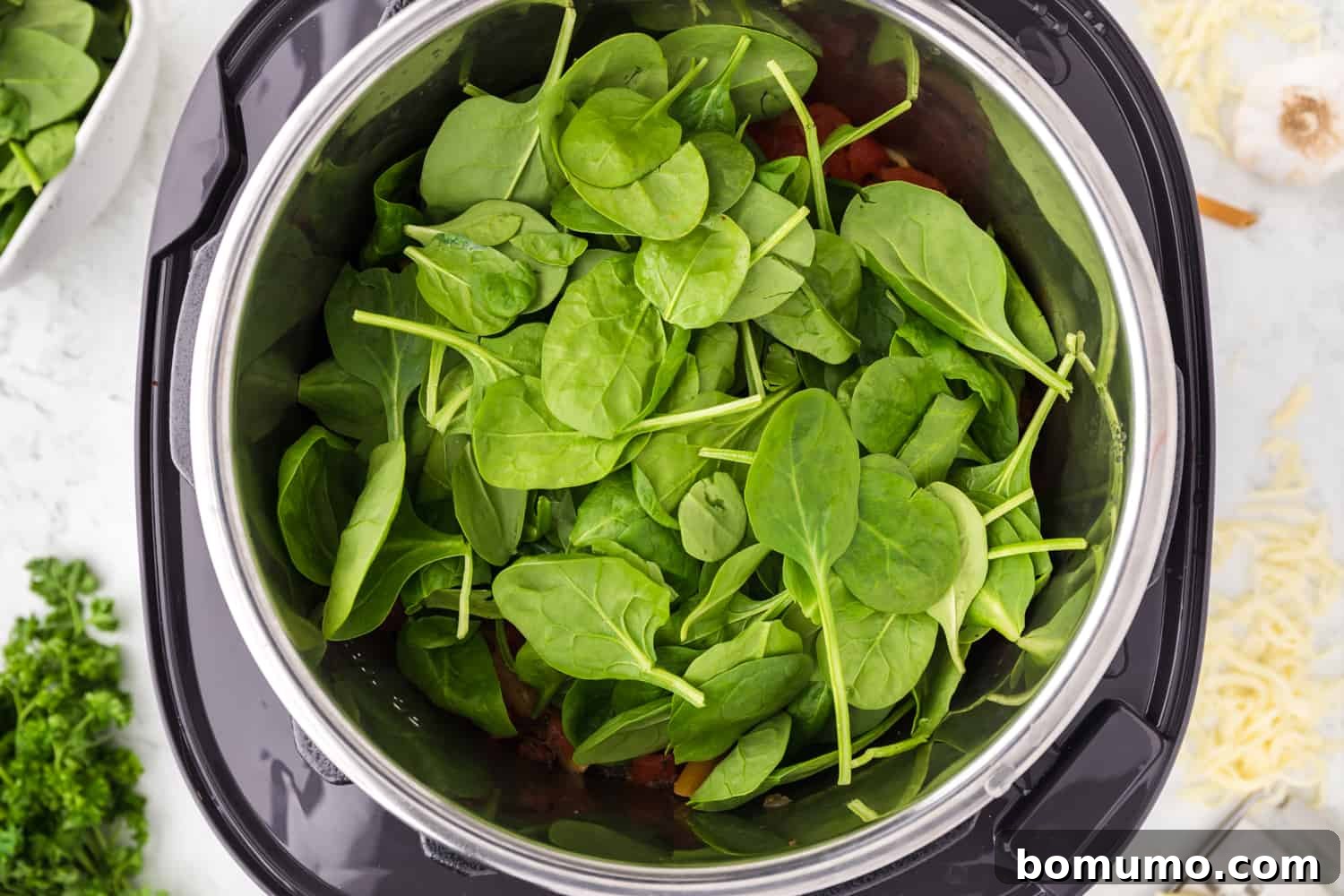 Fresh, unwilted baby spinach added to the cooked pasta in the Instant Pot, ready to be incorporated.