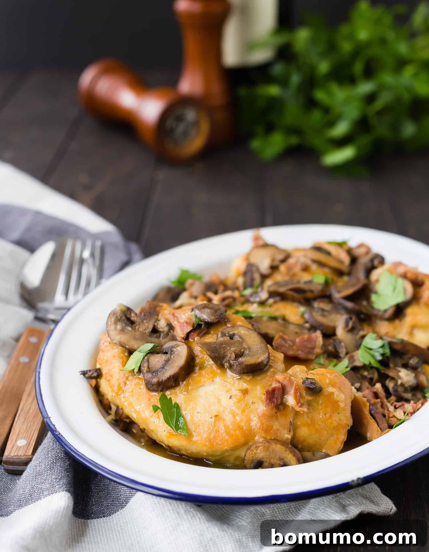 A close-up of tender chicken Marsala, generously topped with fresh green parsley, served on a white plate with a rustic backdrop.