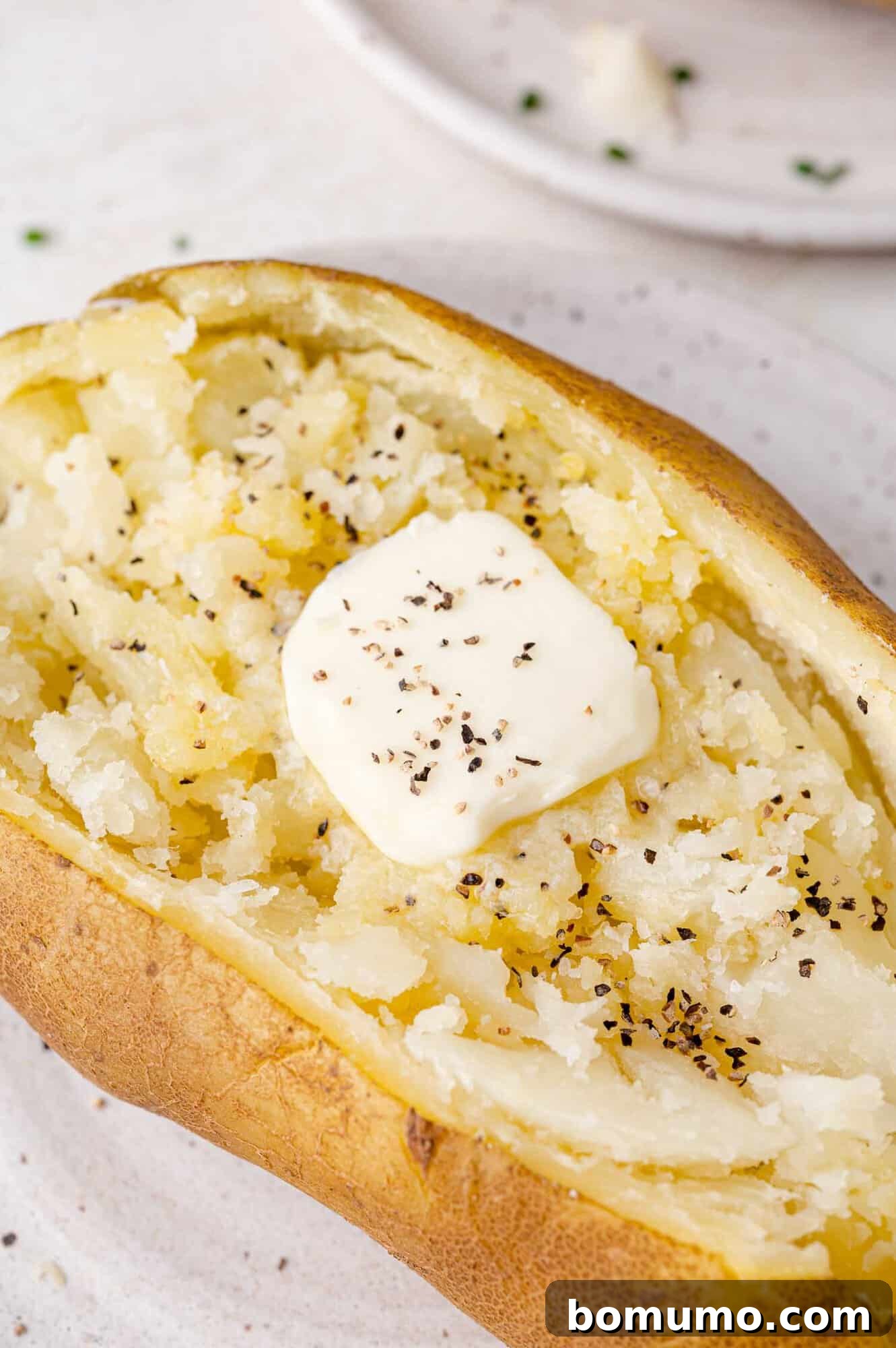 Experience the speed and convenience of making Instant Pot Baked Potatoes for remarkably fluffy results. Once you try this super-fast method, it will quickly become your preferred way to prepare this classic comfort food. Dive into the easy recipe tonight and discover a new weeknight dinner staple! A perfectly baked potato with gently cracked skin, adorned with a melting pat of butter and a sprinkle of freshly ground black pepper, served on a white plate. This image evokes the warmth and comfort of a home-cooked meal, highlighting the delightful simplicity of Instant Pot baked potatoes.