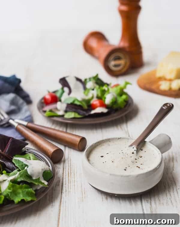 Parmesan Peppercorn Dressing in a small bowl, with a salad in the background. A creamy, cheesy dressing that's lighter than traditional ranch.