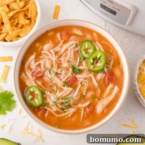 A cozy bowl of chicken chili, beautifully topped with fresh sliced jalapeños and fragrant chopped herbs, presented next to inviting bowls of shredded cheese and crispy tortilla strips, ready to be enjoyed.