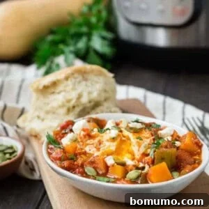 Small white oval bowl filled with tomato sauce, cubed squash, an egg, feta cheese, and pepitas.