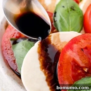 Balsamic glaze being artfully drizzled over a vibrant Caprese salad, ready to serve.
