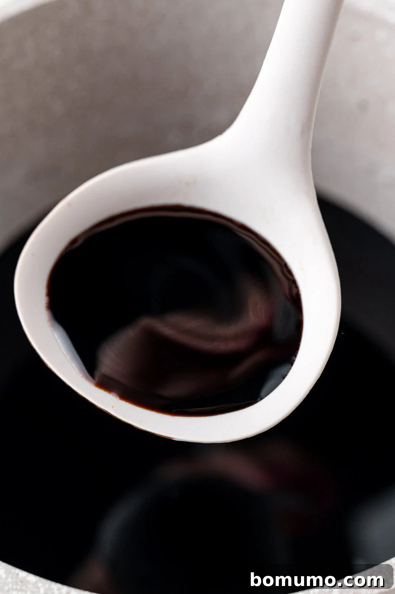 Perfectly thickened balsamic glaze captured in a small ladle, illustrating its rich consistency.