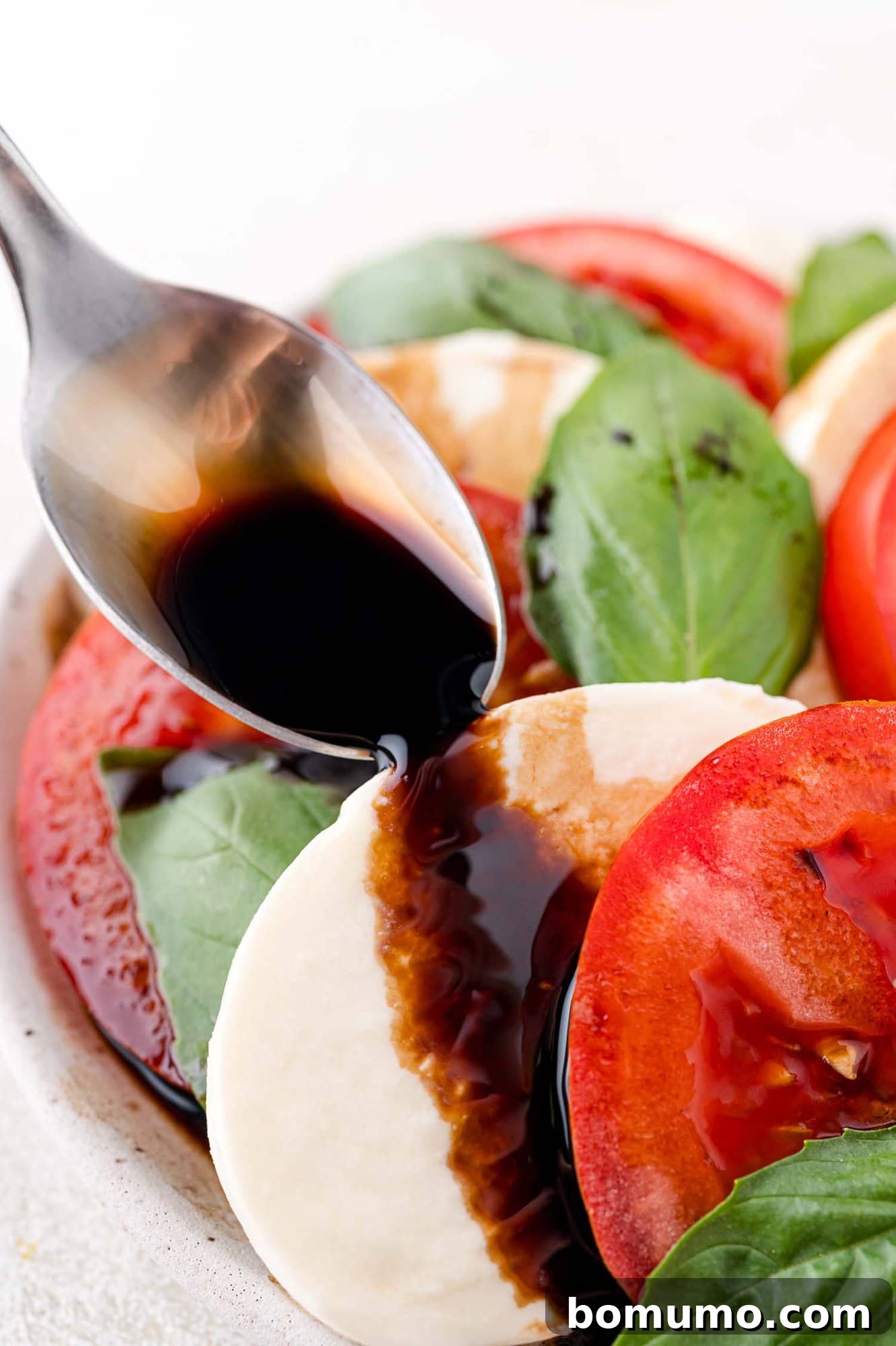 Lustrous balsamic glaze being elegantly drizzled onto a vibrant Caprese salad, enhancing its appeal.