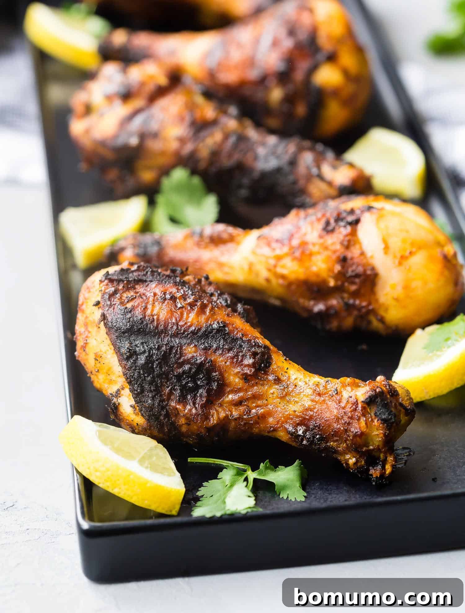 Grilled chicken shawarma drumsticks on a black platter with lemon wedges.