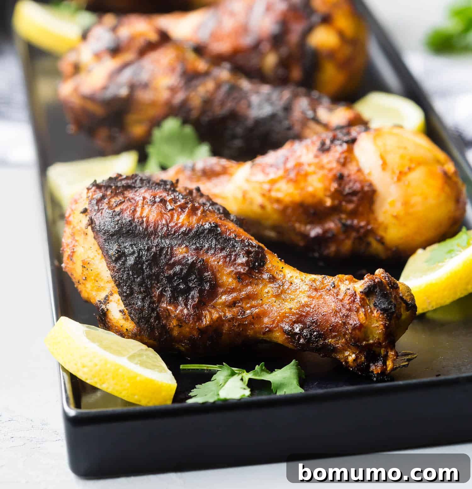 Close-up of grilled chicken shawarma drumsticks on a black platter.