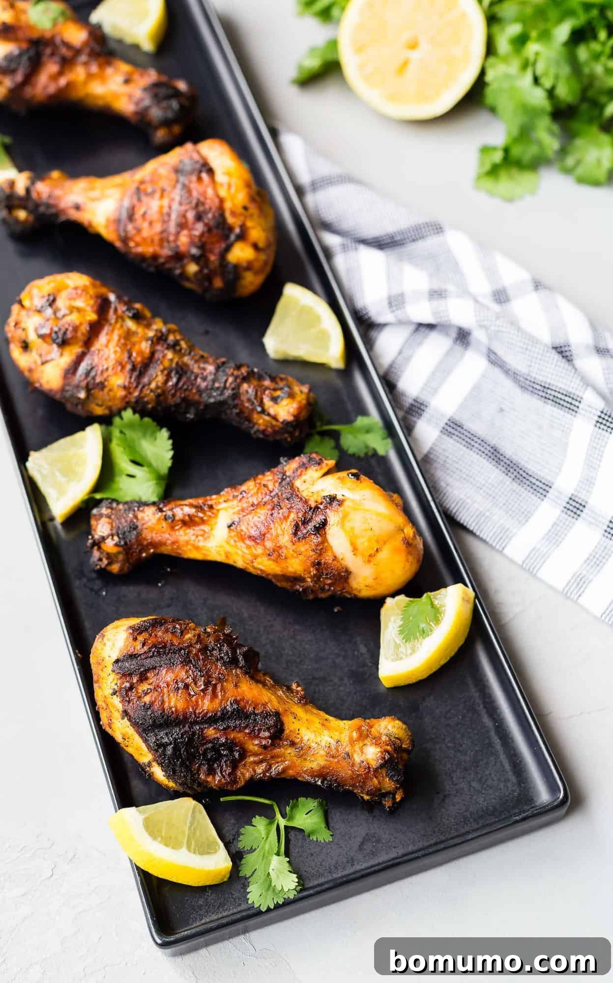 Overhead view of grilled chicken drumsticks on a black platter.