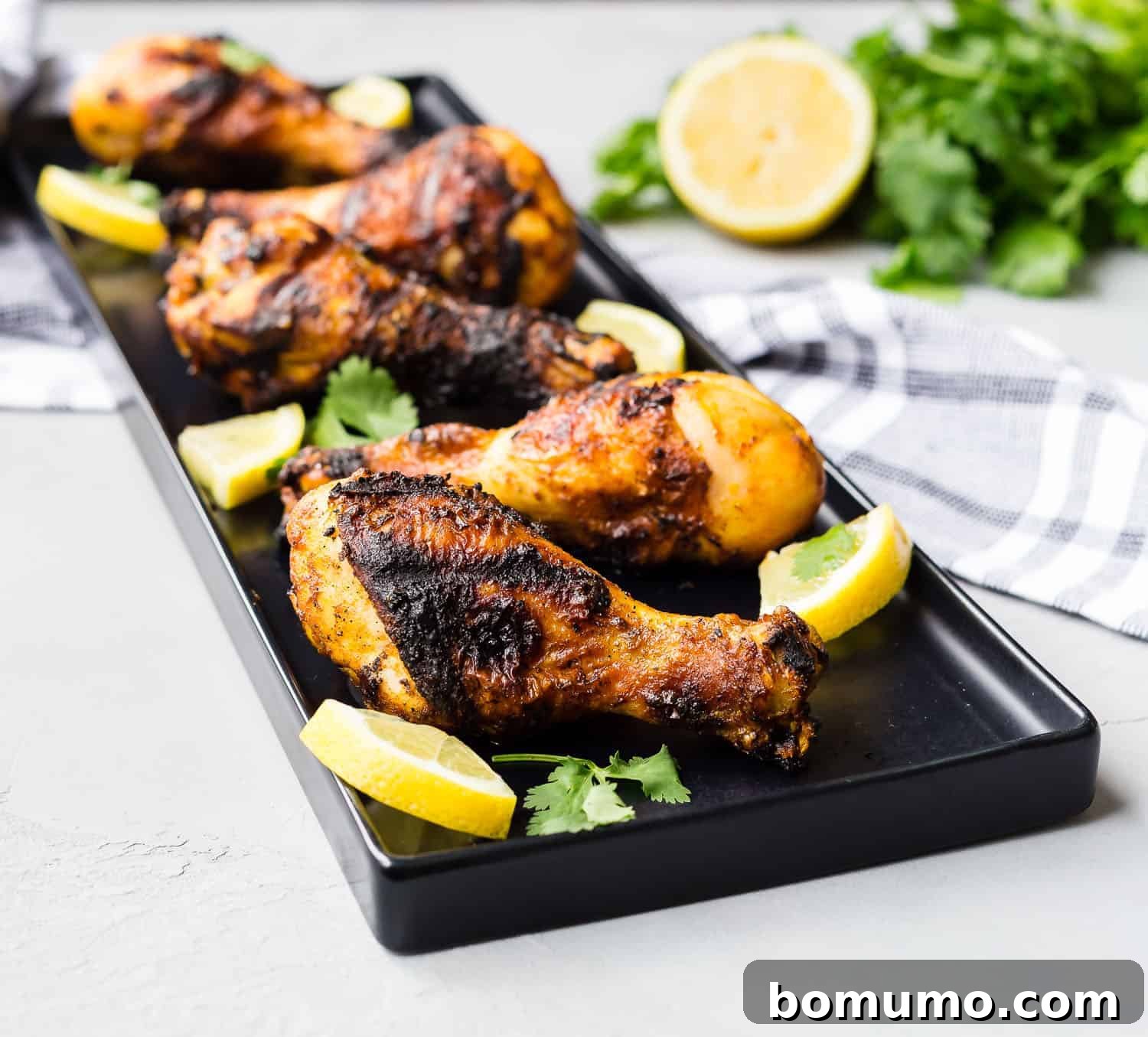 Close-up of grilled chicken drumsticks on a black platter.