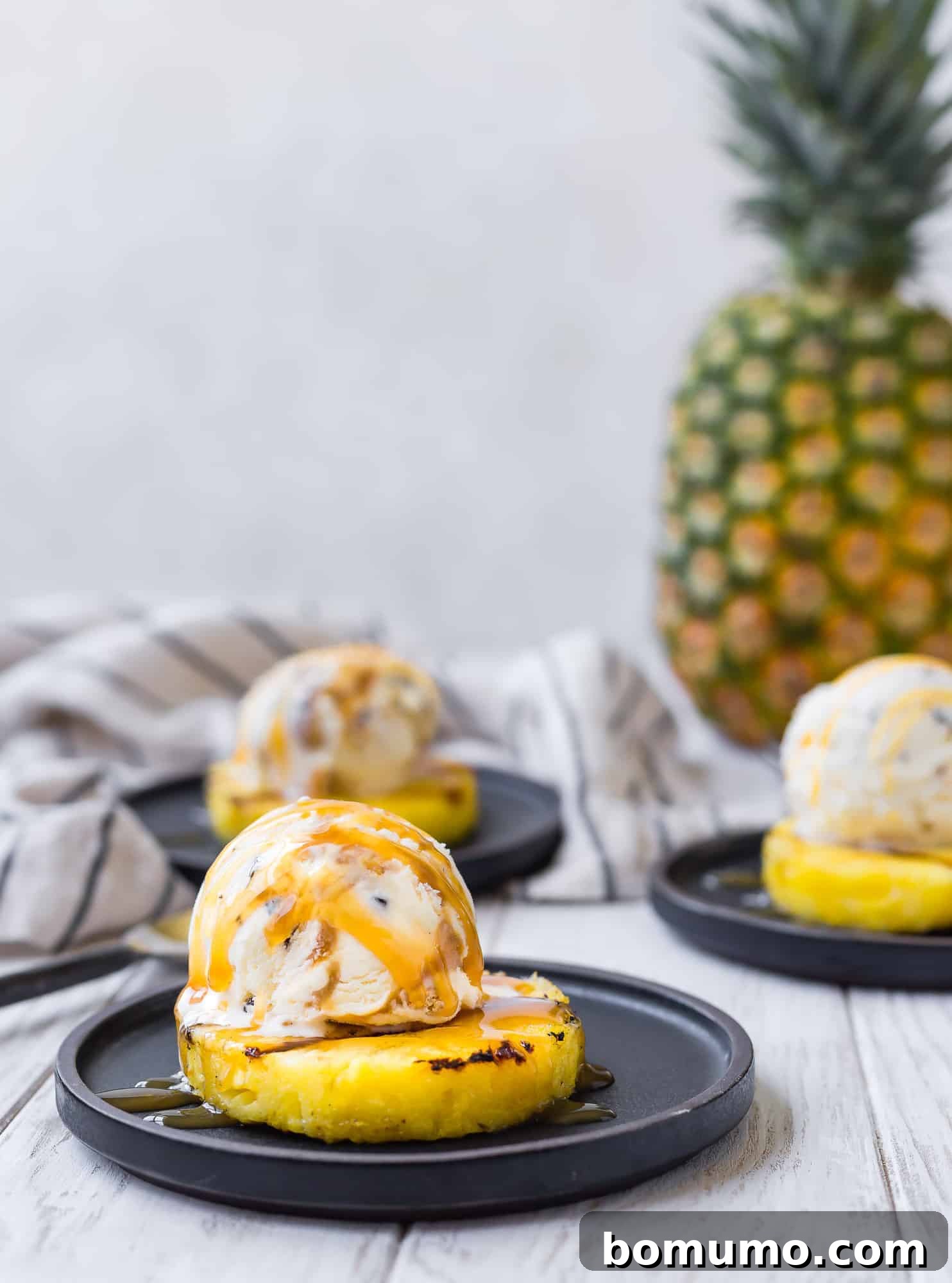 Grilled pineapple topped with a generous scoop of rich caramel toffee crunch ice cream and a luscious drizzle of caramel sauce, embodying the ultimate summer dessert experience.