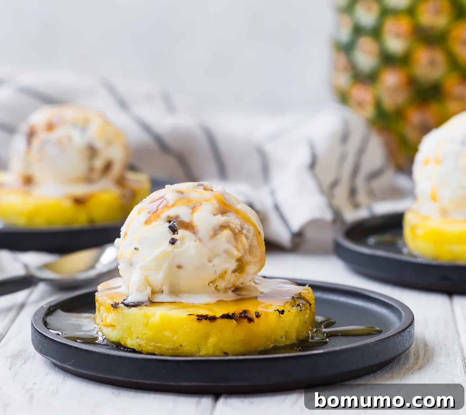 Two artfully arranged servings of grilled pineapple with ice cream, one in sharp focus in the foreground, and another subtly blurred in the background, showcasing the dessert's delicious and inviting appeal.